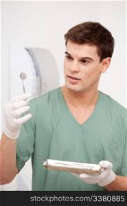 Young male dentist inspecting mirror and holding stainless steel tray