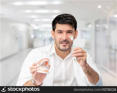 Young male dentist showing toothbrush and denture in dental clinic. Selective focus at the toothbrush.
