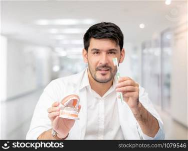 Young male dentist showing toothbrush and denture in dental clinic. Selective focus at the toothbrush.