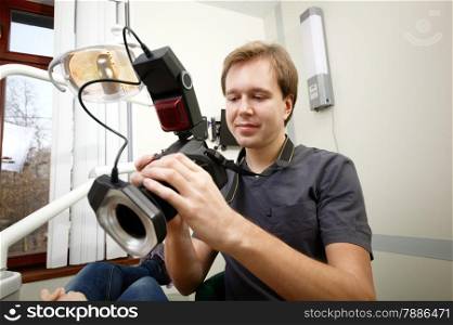Young male dentist with camera making shots of patients smile after treatment