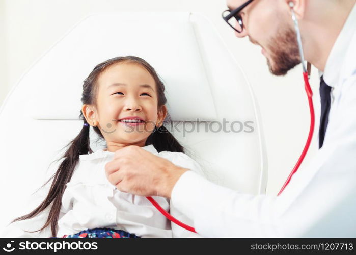 Young male doctor examining little kid in hospital office. The kid is happy and not afraid of the doctor. Medical children healthcare concept.. Doctor examining little happy kid in hospital.