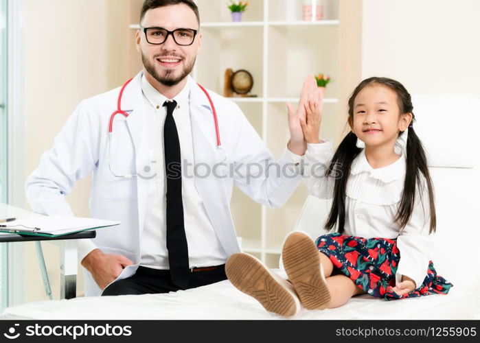 Young male doctor examining little kid in hospital office. The kid is happy and not afraid of the doctor. Medical children healthcare concept.