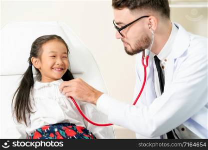 Young male doctor examining little kid in hospital office. The kid is happy and not afraid of the doctor. Medical children healthcare concept.. Doctor examining little happy kid in hospital.