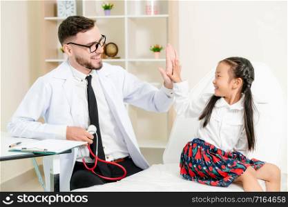 Young male doctor examining little kid in hospital office. The kid is happy and not afraid of the doctor. Medical children healthcare concept.. Doctor examining little happy kid in hospital.