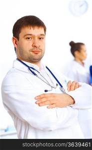 Young male doctor in white uniform with collegues on the background