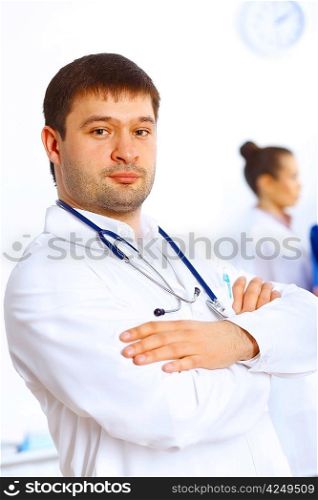 Young male doctor in white uniform with collegues on the background