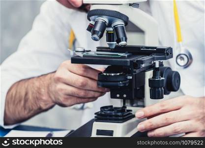 Young male doctor working using microscope in hospital laboratory. Medical and medicine technology research and development concept.
