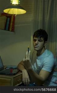 Young male drug addict holding syringe at home