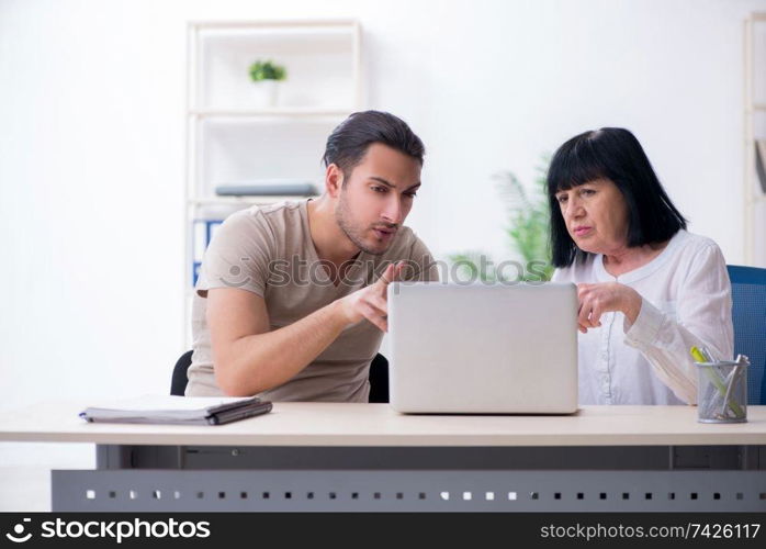 Young male employee explaining to old female colleague how to use computer. Young male employee explaining to old female colleague how to us