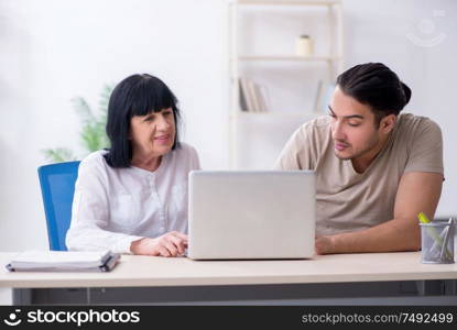 Young male employee explaining to old female colleague how to use computer. Young male employee explaining to old female colleague how to us