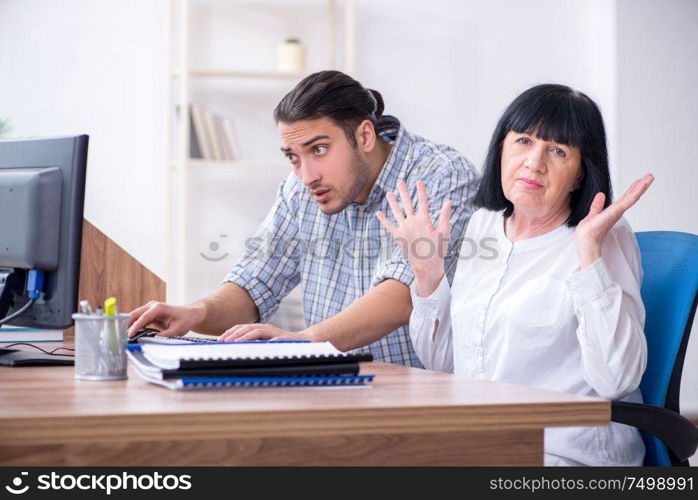 Young male employee explaining to old female colleague how to use computer. Young male employee explaining to old female colleague how to us