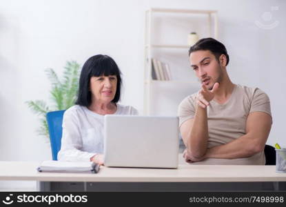 Young male employee explaining to old female colleague how to use computer. Young male employee explaining to old female colleague how to us