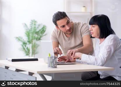 Young male employee explaining to old female colleague how to use computer. Young male employee explaining to old female colleague how to us