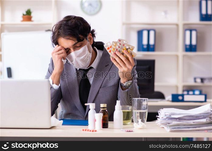 Young male employee suffering at workplace . Man with flu working in the office