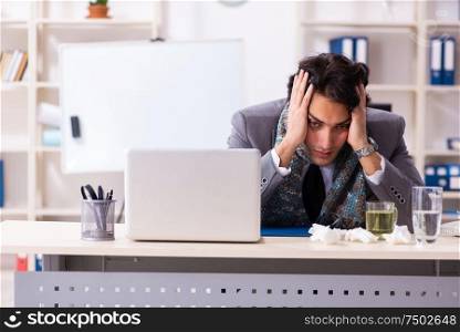 Young male employee suffering at workplace. Man with flu working in the office