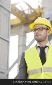 Young male engineer wearing hard hat looking away at construction site