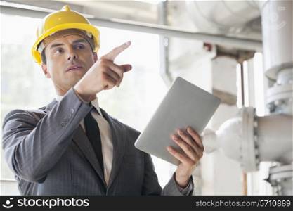 Young male engineer with digital tablet pointing away in industry