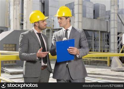 Young male engineers with clipboard discussing at construction site