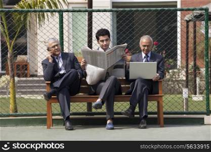 Young male executive reading newspaper while sitting among senior executives on bench