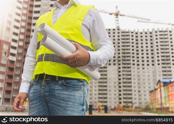 Young male foreman holding rolled blueprints