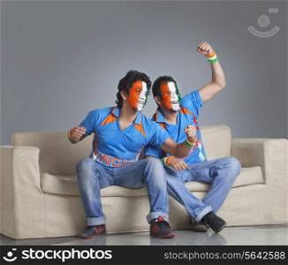 Young male friends with face painted in tricolor cheering while sitting on sofa