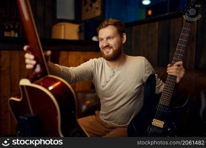 Young male guitarist choosing musical instrument between electric or acoustic guitar to play. Young guitarist choosing electric or acoustic guitar