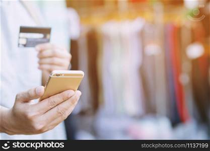 young male hands holding credit card and using mobile smart phone Standing in front of the clothing store. Online shopping purchase Sell or Payment.