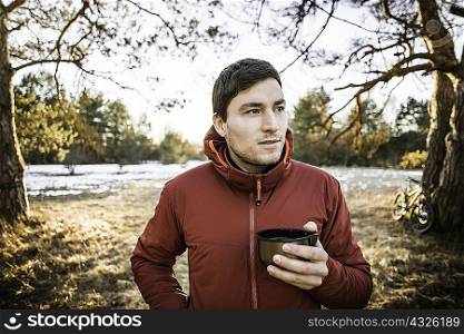 Young male hiker drinking coffee in lakeside forest