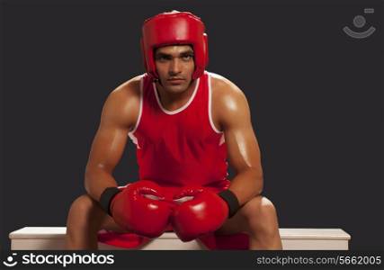 Young male Indian boxer sitting on bench isolated over black background
