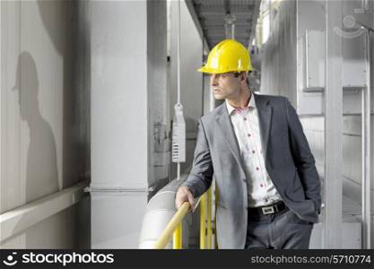 Young male manager wearing hard hat looking away in industry