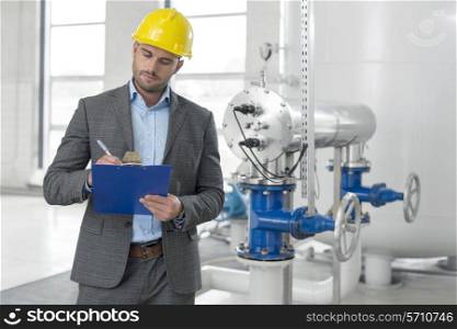 Young male manager writing on clipboard in industry