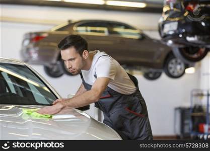Young male mechanic cleaning car in repair shop