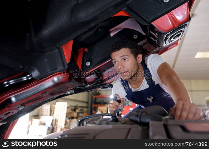 young male mechanic inspecting industrial vehicle with torch