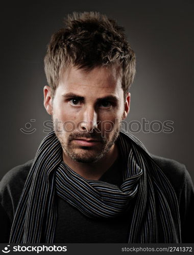 Young male model wearing a dark shirt and striped scarf. He has a serious expression and is shot on a gray background.. Commercial Photography