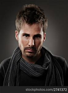 Young male model wearing a dark shirt and striped scarf. He has a serious expression and is shot on a gray background.. Commercial Photography