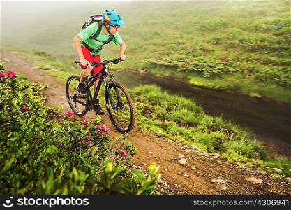 Young male mountain biker cycling next to stream