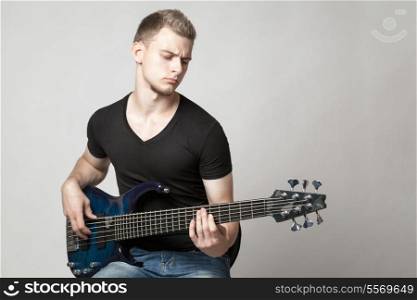 young male musician playing a six-string bass guitar isolated on light background