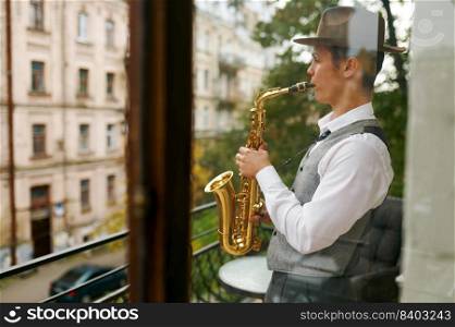 Young male musician practicing saxophone in balcony at home. Inspired saxophonist playing music. Young male musician practicing saxophone in balcony at home