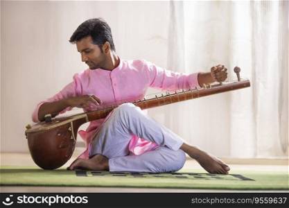 Young male musician tuning his sitar while sitting in living room