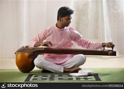 Young male musician tuning his Tanpura while sitting in living room