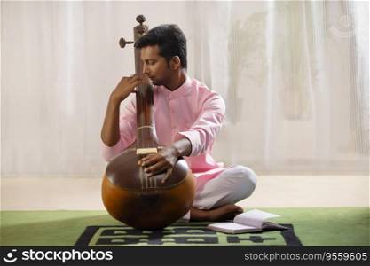 Young male musician tuning his Tanpura while sitting in living room