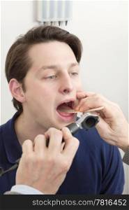 Young male patient getting his tongue and mouth checked for infection by doctor