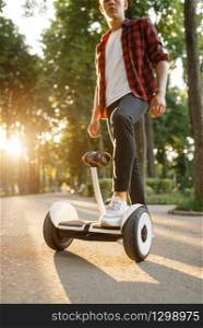 Young male person riding on gyroboard in summer park. Outdoor recreation with electric gyro board. Eco transport. Electrical gyroscope vehicle. Young male person riding on gyroboard in park