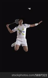 Young male player jumping to hit shuttlecock with racket over black background