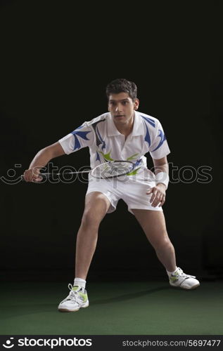 Young male player playing badminton over black background