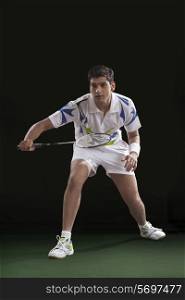 Young male player playing badminton over black background