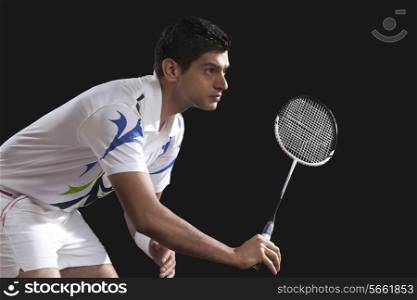 Young male player with racket playing badminton isolated over black background