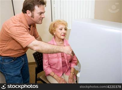 Young male poll worker assisting a senior woman with a new touch screen voting machine.