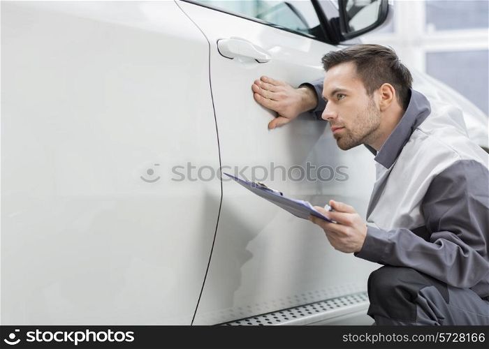 Young male repair worker examining car in automobile repair shop