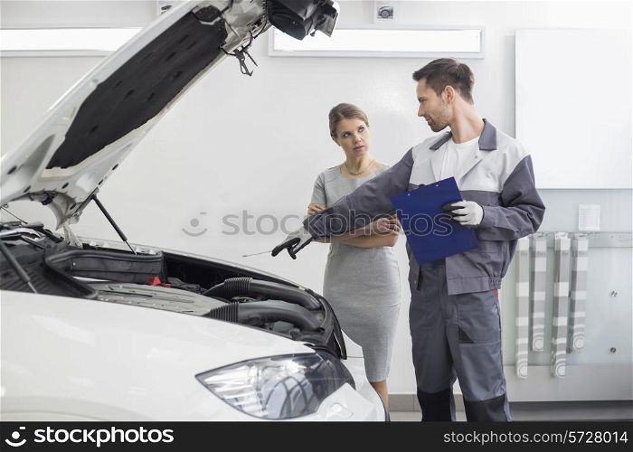 Young male repairman explaining car engine to female customer in automobile repair shop